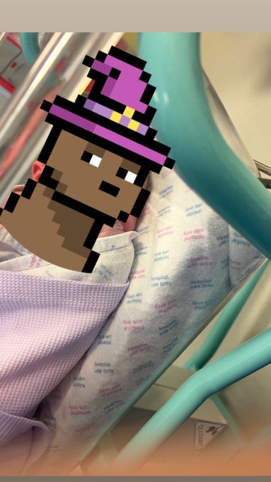 A hospital scene where an infant in a baby blanket lies in a teal hospital crib, overlaid with a pixel art sticker of a character wearing a purple wizard hat.