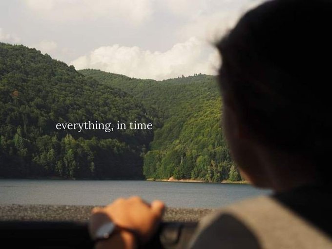 A scenic photograph of a person looking out over a lake toward forested mountains, with the text overlay 'everything, in time'.