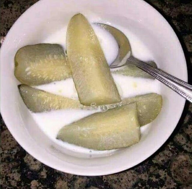 A white bowl contains several pieces of green, wedge-cut fruit in a milky liquid, with a silver spoon resting in the bowl.