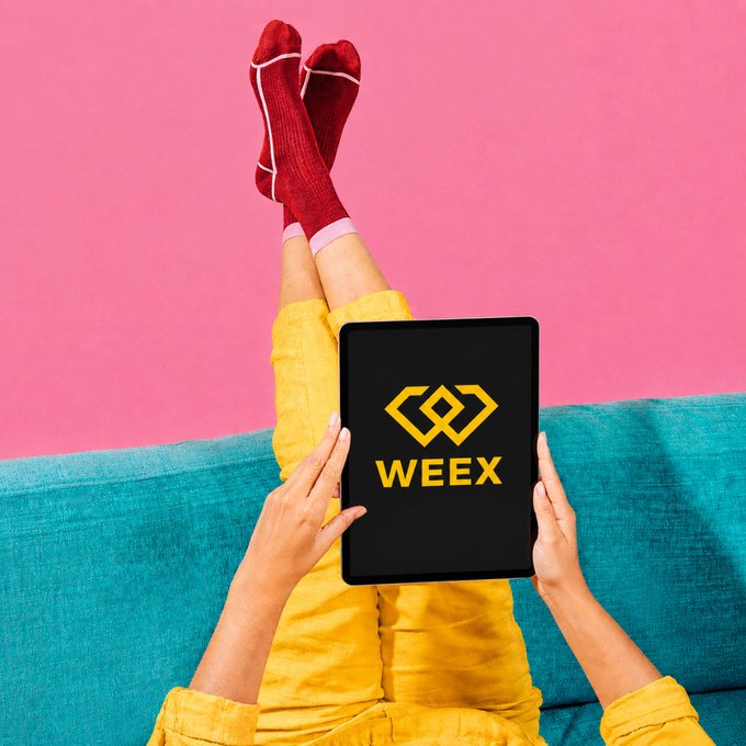 A person in yellow pants and red socks relaxes on a teal couch while holding a tablet displaying the WEEY logo against a pink background.