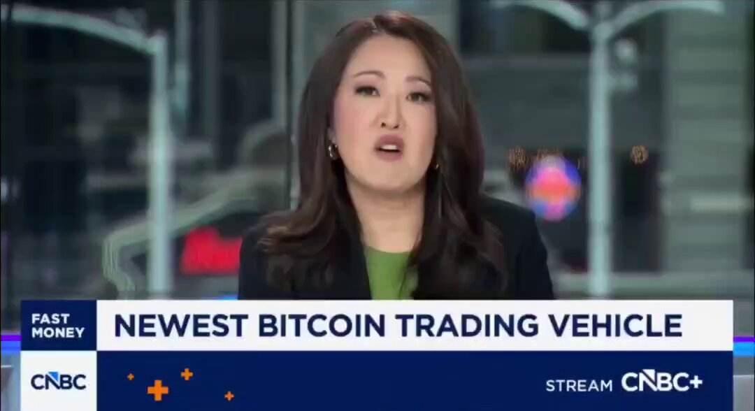 The image features a woman sitting at a desk, talking about Bitcoin trading vehicles. The text on the screen reads "Newest BitCoin Trading Vehicle Stream Cbc+", which indicates that she is discussing the latest developments in Bitcoin trading. The woman's facial expression and body language suggest that she might be sharing her thoughts or opinions on this topic with viewers of the image.