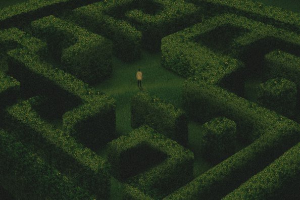 An aerial view shows a solitary figure walking through a dark green hedge maze.