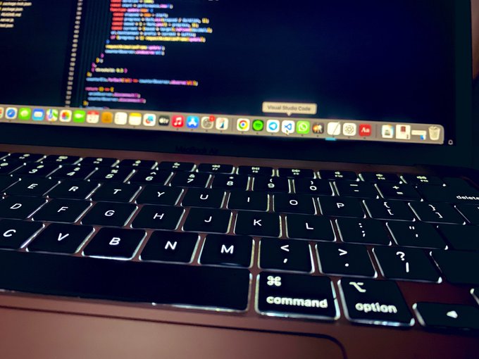 A close-up view of a laptop keyboard with the screen displaying Visual Studio Code with colorful code lines against a dark background.