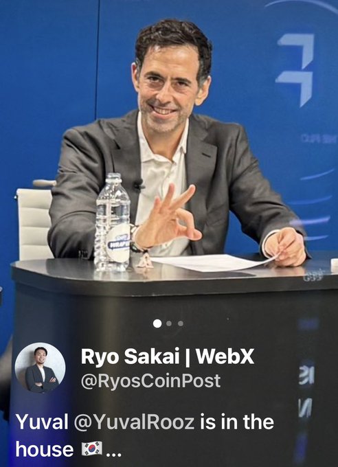 A Twitter screenshot from Ryo Sakai (@RyosCoinPost) of WebX showing a man in a gray suit smiling and gesturing during what appears to be a panel discussion, with the caption "Yuval @YuvalRooz is in the house".