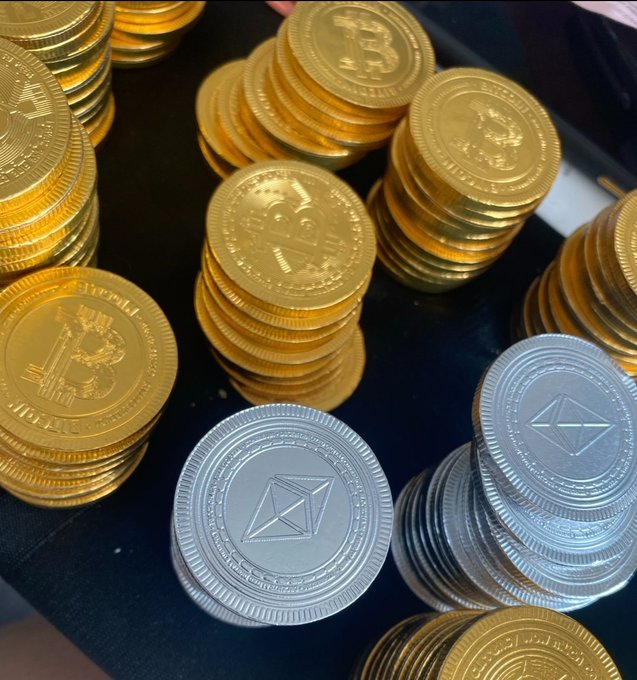 Stacks of gold Bitcoin and silver Ethereum commemorative coins are piled together on a dark surface. The image playfully represents the "token budget" she jokes about saving up for, with the mix of crypto collectibles symbolizing the digital assets her future husband could freely invest in.