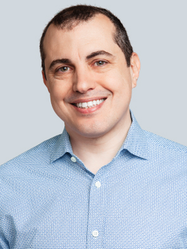 The image shows a smiling man in a light blue button-down shirt against a light blue background, presented in a polished, professional headshot style. Given the post's comparison about a Bitcoin spokesperson "we deserve vs. the one we got," the clean-cut, approachable appearance of the man appears to be juxtaposed—humorously or critically—against an unflattering implied alternative spokesperson figure.