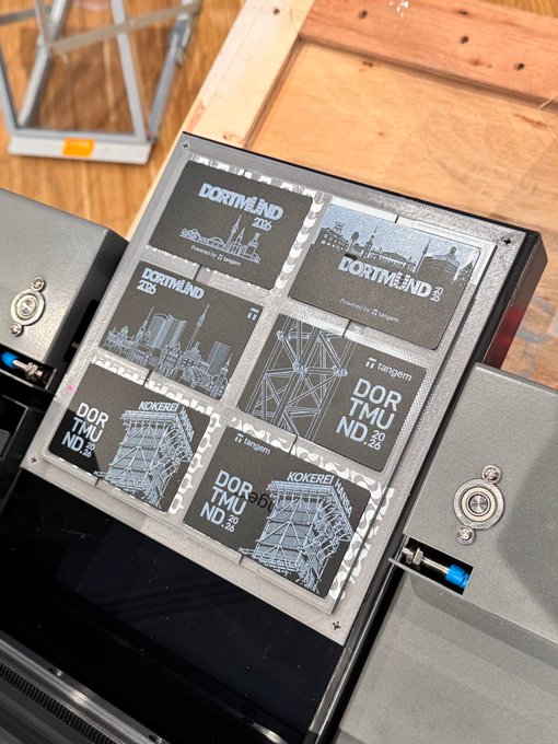 A customized Tangem cold wallet featuring black-and-white Dortmund skyline illustrations alongside the "DOR 2.0," "DOR 205," and "KOKEREI" branding sits open on a wooden surface, showcasing the conference-specific design mentioned in the post. The sleek device displays the custom artwork on multiple cards arranged within its protective case.