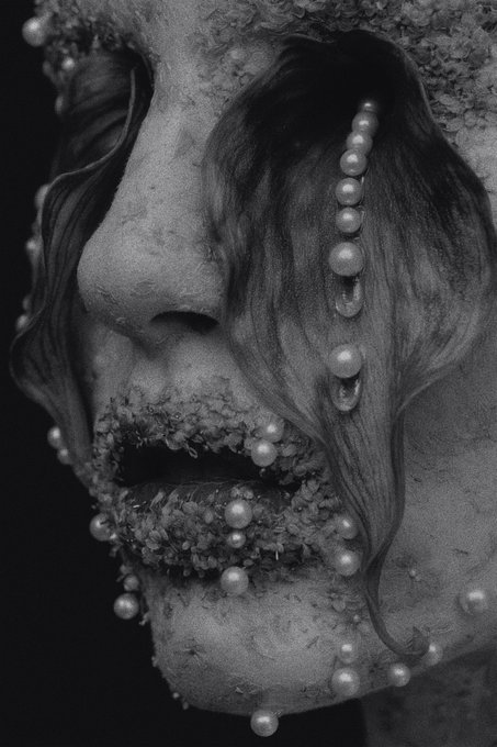 A black and white close-up of a stone or clay sculpture showing a face with closed eyes and serene expression, adorned with small pearls and floral arrangements cascading from the eye and covering the lips, evoking a melancholic or tearful aesthetic that aligns with the post's title "9.cry" by artist cora.
