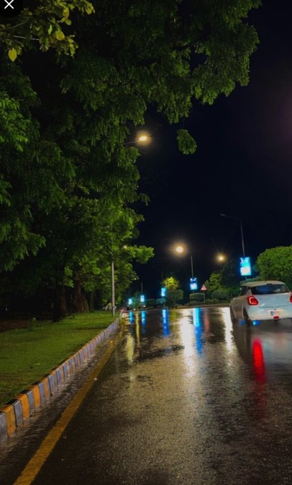The image shows a street at night with rain falling, reflecting off of the wet pavement. There are two cars driving down the road, one white car and one black car. The scene also includes trees lining the street, adding to the overall ambiance. The caption in the image reads "gn good night, Is sleeping late actually good or not? @NomismaNetwork Today's cooking mood @useTria". This statement seems unrelated to the main subject of the photo and could be a random comment made by someone who took the picture.

The image does not provide enough information about the post to determine if it is relevant, accurate, or informative.