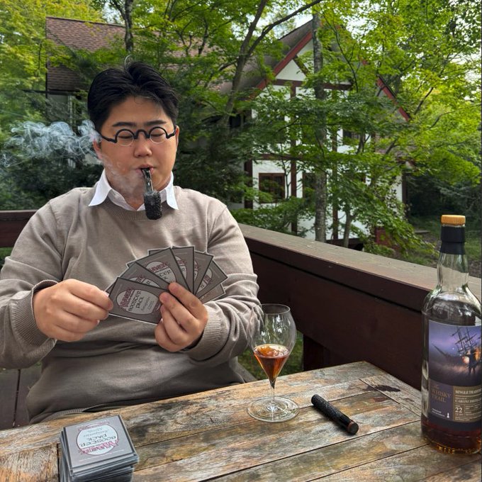 A man wearing glasses and a beige sweater sits at a wooden outdoor deck table, calmly puffing a Sherlock Holmes-style pipe while fanning out a hand of coasters—one reading "Eagle Rare"—next to a snifter of bourbon, a cigar, and a bottle of "Smooth Ambler" whiskey, celebrating his $2K turning into $25K in under two weeks with a refined gentleman's retreat.