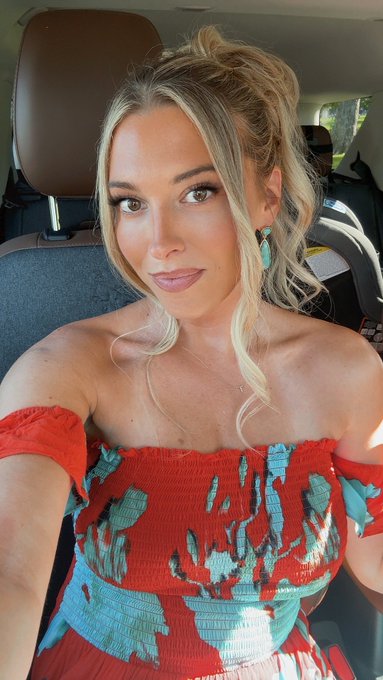 A woman with blonde hair styled up takes a selfie in a car, wearing a red and blue floral off-the-shoulder top with turquoise statement earrings. The image likely accompanies her promo code "TAYLOR" for $20 off, serving as a personal branded post to promote her partnership with Polymarket.