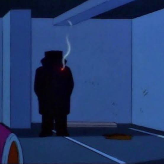 A shadowy figure in a trench coat and hat stands in a dimly lit parking garage, smoking a cigarette with only the glowing tip visible against the dark silhouette. The image evokes the ominous "men in black" trope, fitting the post's warning that someone will mysteriously appear to notify you of the market cycle bottom—an elusive, almost conspiratorial signal.
