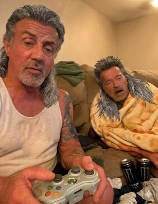 The image shows two men sitting on a couch, one holding a game controller while another man has his head wrapped in a blanket with long hair. The background includes a wall clock and various objects such as a can of Monster energy drink and a soda can.