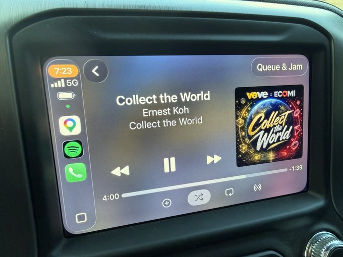 A car's infotainment screen displays the song "Collect the World" by Ernest Koh playing through Spotify, with the $OMI (ECOMI) digital collectibles album artwork visible on the right side. The post connects perfectly with the image, capturing the moment of jamming to this Web3-inspired track during the morning carpool.