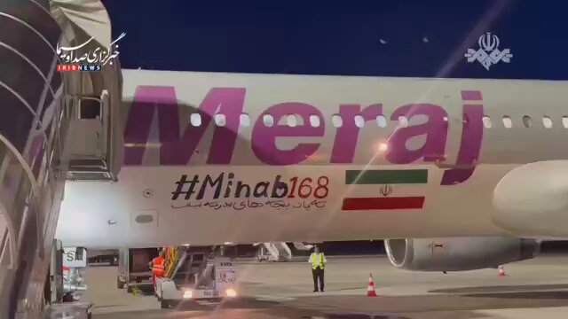 The image features a large airplane with the words "Mera" written on its side, along with some text that reads " Bitcoins". The airplane appears to be parked at an airport, as there are people walking around near it. A person is standing next to the plane and another person can be seen further away from the aircraft. Additionally, a suitcase is visible in the scene, suggesting that someone might have recently arrived or is preparing for departure.