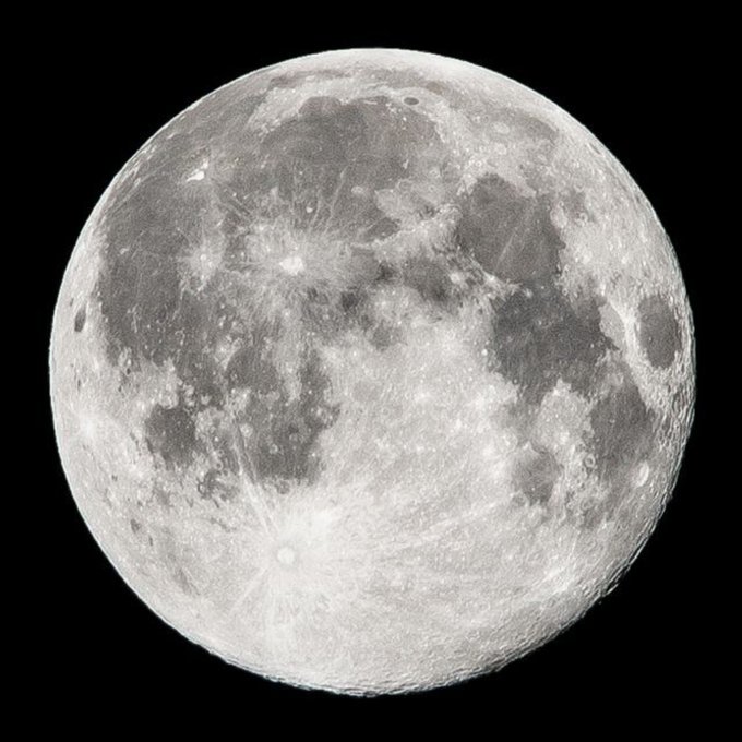 A detailed black and white photograph of a full moon showing its craters and surface features against a black background.