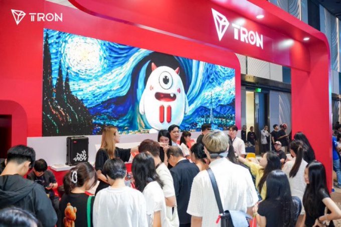 A crowd gathered at a red TRON booth displaying a large screen with a Van Gogh-style 'Starry Night' background and a white cartoon mascot character.