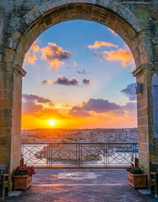 A scenic view of a sunset over a harbor and city, framed by a large stone archway with potted flowers on the balcony.
