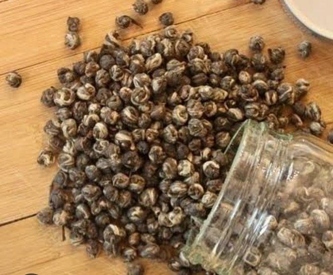 A pile of small dried snail or shell-like objects scattered on a wooden surface next to a clear plastic bag.