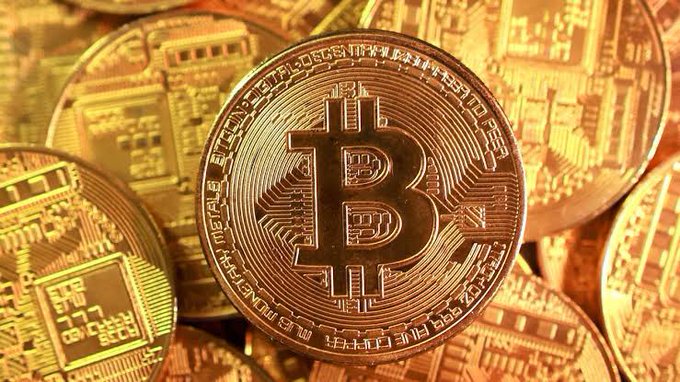 Golden Bitcoin physical tokens are stacked together, prominently displaying the iconic "B" symbol and inscriptions including "BITCOIN DIGITAL DECENTRALIZED PEER TO PEER," visually reinforcing Trump's comment about the growing adoption of Bitcoin as a payment method over traditional cash.
