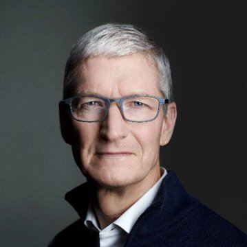 The image shows Tim Cook, Apple's CEO, in a professional portrait wearing glasses and a dark sweater. The caption should describe his appearance while connecting to the post about him leading Apple as a multi-trillion-dollar company and building the future alongside other innovative leaders.