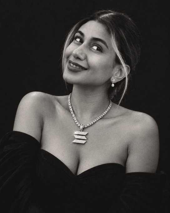 A black-and-white portrait features a smiling woman wearing an elegant diamond necklace and matching earrings, dressed in a dark off-the-shoulder gown.