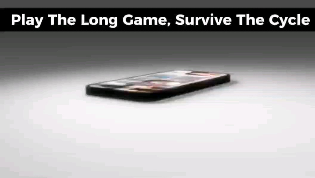 A minimalist image of a smartphone lying on a white surface with the text 'Play The Long Game, Survive The Cycle' displayed in a black banner at the top.