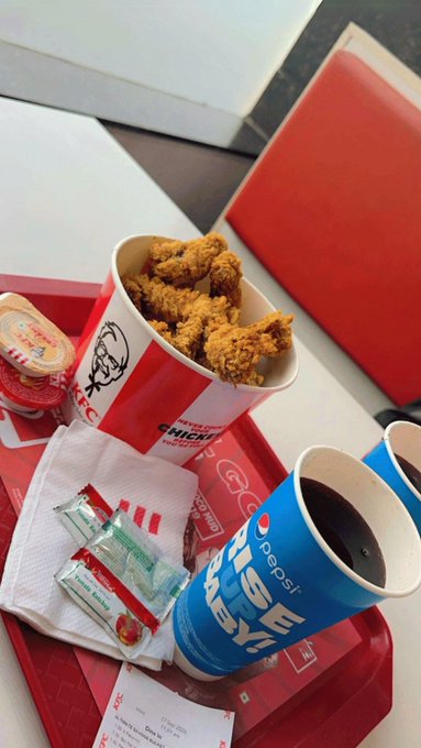 A meal at a fast-food restaurant featuring a bucket of fried chicken, a blue Pepsi cup, condiments, and a receipt on a red tray.