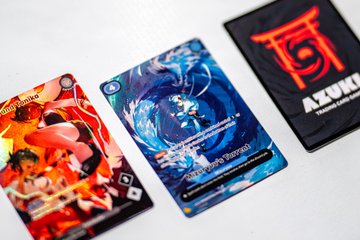 Three Azuki Trading Card Game cards are displayed, featuring vibrant anime-style artwork and the prominent "AZUKI" logo. This image visually complements the post about photographing Azuki TCG cards on a sunny day.