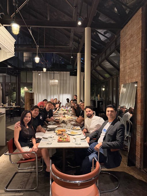 A group of around 15 people gathered around a long dining table for what appears to be a community dinner, with a man in a dark blazer seated at the head of the table. The setting looks like an upscale restaurant or co-working space with high ceilings, exposed beams, and industrial lighting. This image captures one of the social dinners mentioned in the post, showcasing the growth of what started as a small unofficial Solana Thailand meetup in April into a thriving community now organizing coworking sessions, workshops, and gatherings.