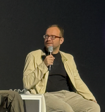 A bespectacled man with a beard, wearing a black t-shirt and beige jacket, speaks into a microphone while seated on stage. The image aligns with the caption, showing Vlad Novakovski, CEO of Lighter, addressing an audience at Korea Blockchain Week 2026 about opportunities in DeFi fixed income markets.