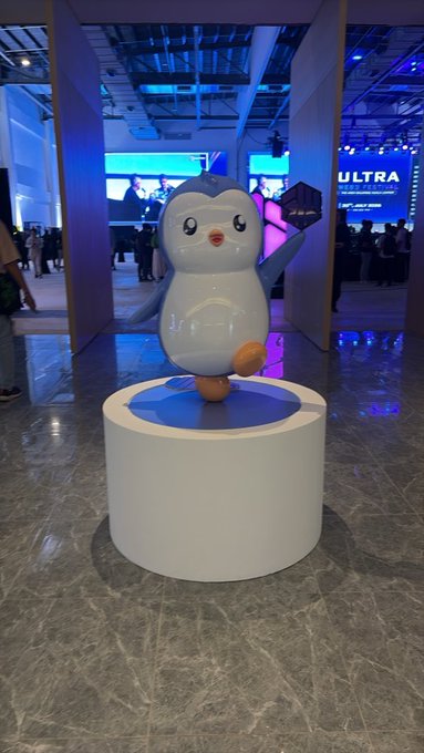 A 3D rendering of a cute cartoon penguin standing on a white cylindrical pedestal in a futuristic or retail environment.