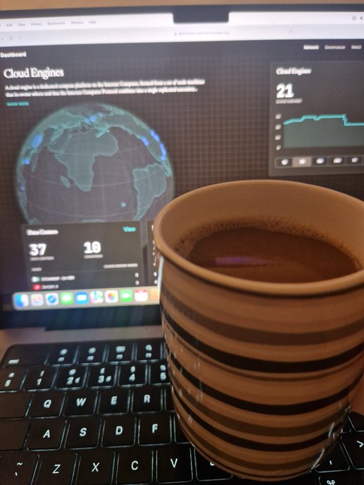A ceramic coffee mug sits on a laptop keyboard in front of a screen displaying a 'Cloud Engines' dashboard with a globe graphic and analytics.