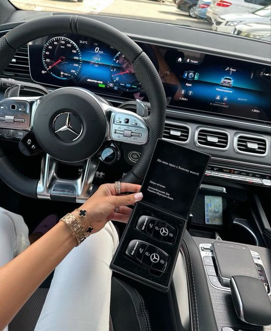 A woman in a Mercedes-Benz (visible "AMG" badge) shows off a luxury gift box containing two Mercedes car key fobs, with the digital dashboard displaying "34.0°C" and various app icons. The image ties to the "Good morning web3, You gm?" post by suggesting a stylish, luxury-lifestyle flex to start the day.