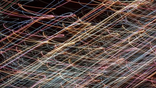 An abstract image featuring colorful light trails in gold, pink, and blue sweeping across a dark background, creating a sense of dynamic motion.