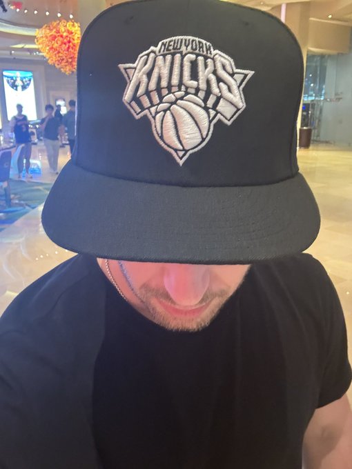 iced coffee with a straw, black New York Knicks cap, and a blurred background of people.