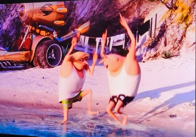 Two animated characters in tank tops and shorts dance joyfully on a beach with arms raised in front of a stylized truck parked near rocky cliffs.
