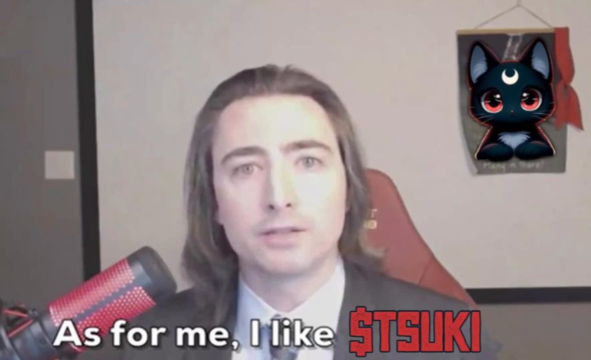 The image features a man with long hair wearing a suit, sitting behind a microphone. The caption of the image reads "$GME people: debunk this. $TSUKI posted 1 day, 1 hour, 1 minute before Roaring Kitty returned from a 3-year absence." This post seems to be about a meme featuring a cat and the name "TSuki" written on it. The caption also mentions that the meme was posted by someone named RK.