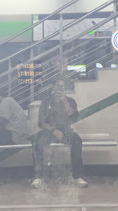 A person sitting on a bench in what appears to be a train station or transit area, partially obscured by glare, with digital text overlays showing 'WT:4334mm', 'ST:1108mm', and 'EC:213mm'.