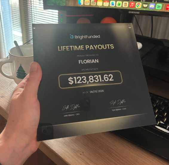 A hand holding a 'BrightFunded' Lifetime Payouts certificate awarded to 'FLORIAN' for $123,831.62 as of 06/01/2026, signed by CEO Jelle Olijslagers and COO Ilya Vygotsky, displayed near a monitor.