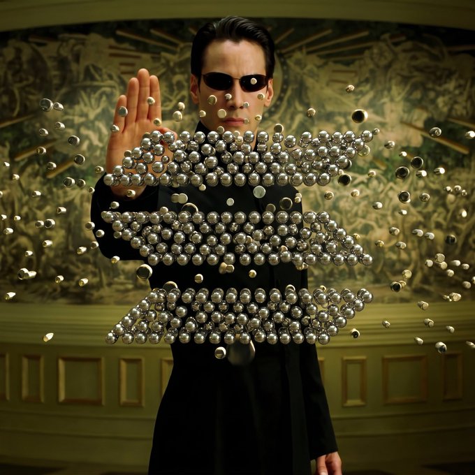 The image features a person dressed as Superman, wearing black attire with goggles, standing behind a display of large beads that look like bullets. The scene suggests an action-packed moment, possibly related to the film "Solana". However, there are no discernible texts or additional objects in the image besides the superhero figure and the bead display.