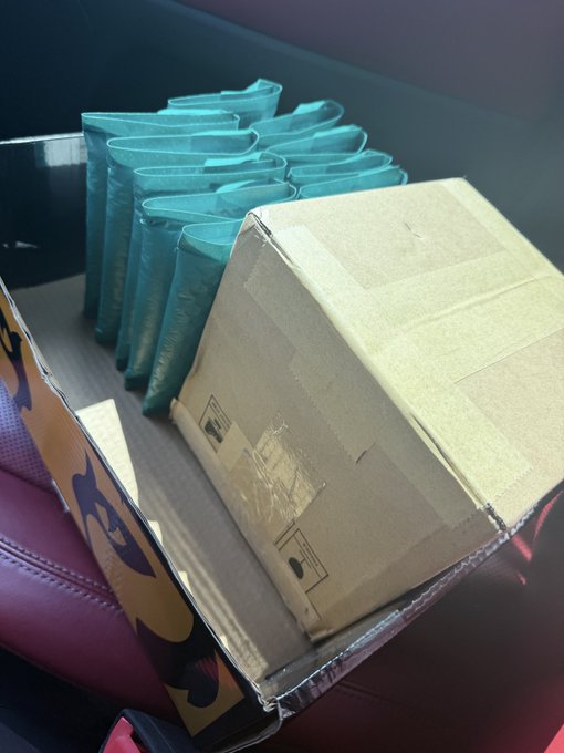 A photograph showing several teal padded mailers and a brown cardboard box resting on what appears to be a desk or chair surface.