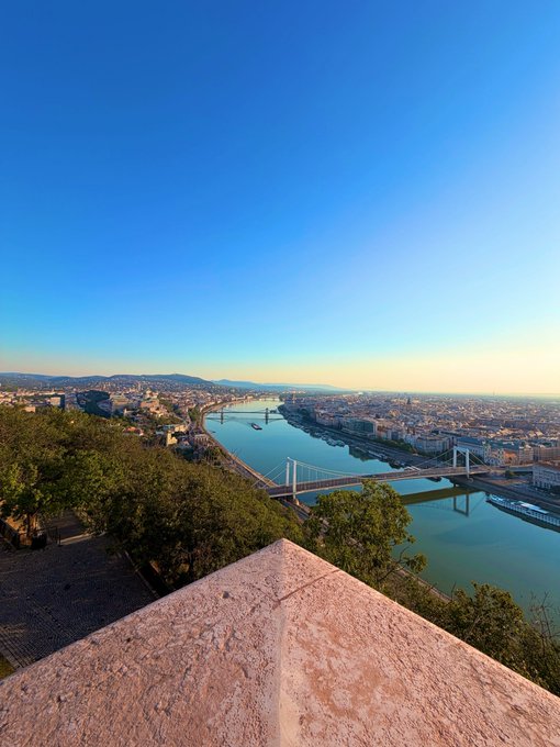 A scenic overlook of Budapest showing the Danube River, the Liberty Bridge (Szabadság híd), and the Chain Bridge, with the Buda Castle district visible on the left.