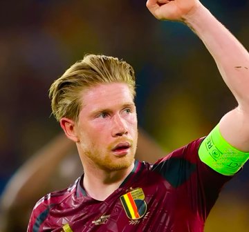 Kevin De Bruyne, the Belgian midfielder, is shown wearing the Belgium national team jersey with his arm raised in celebration, while the caption humorously references his apparent success in farming $POLY cryptocurrency alongside his football career.