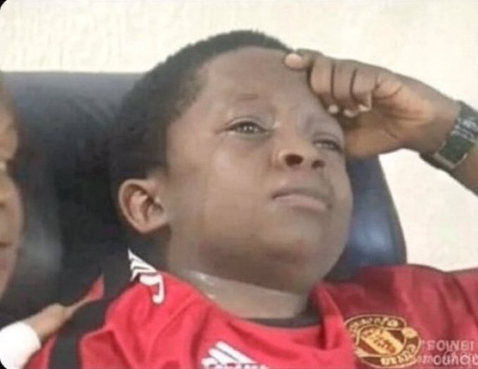 A young man in a red and black soccer jersey sitting with his hand on his forehead, looking distressed or contemplative.