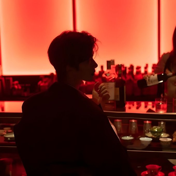A person silhouetted against a red-lit backdrop sits at a bar with bottles in the background, fitting a late-night "gm" greeting vibe for an upcoming giveaway announcement.