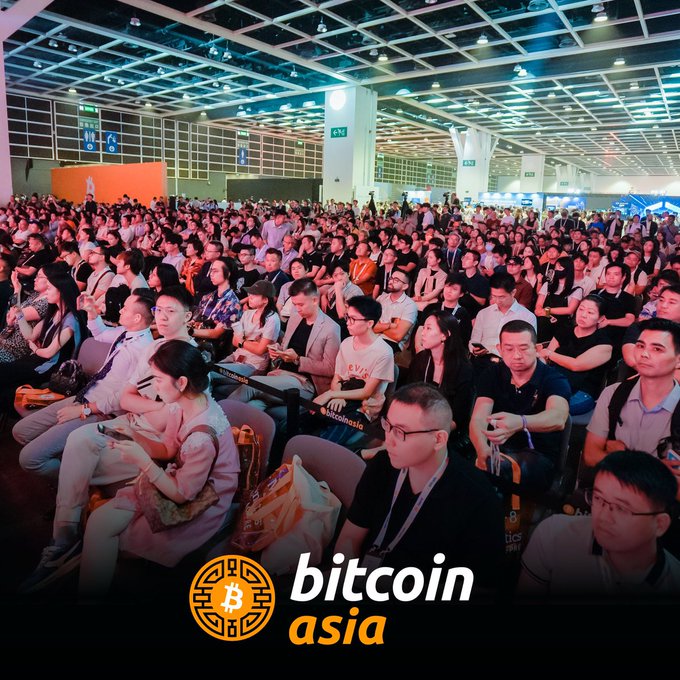 A large crowd attends a Bitcoin Asia conference in a spacious venue with overhead signage directing attendees to halls 5A and 5B, while the image displays the Bitcoin Asia logo with the tagline "bitcoin asia" at the bottom, promoting the upcoming networking event.