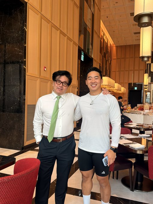 Two men pose for a photo in an upscale restaurant with wood-paneled walls and elegant lighting—one wearing a white shirt with a green tie, and the other in a white athletic shirt and black shorts. The image appears to relate to the post's reference to a leveraged $ETH play associated with Fundstrat ($BMNR), suggesting a casual meeting possibly connected to crypto or financial discussions.