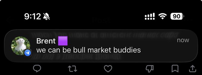 A smartphone notification from "Brent" sent "now" reads "we can be bull market buddies," displayed over a dimmed Reddit-like feed where faint text references "Inu" and "AI," tying the bullish market camaraderie message to the underlying "Artificial Inu" AI-related content.
