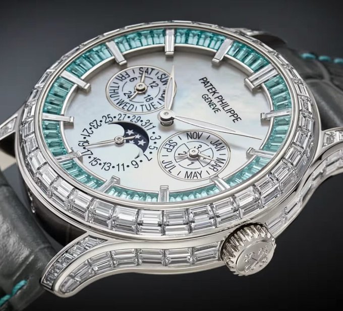 The image features a silver watch with blue gemstones, which appears to be a Rolex watch. It has a black band that contrasts with its white face. The watch's design includes a moon phase indicator, suggesting that it may have an additional function beyond telling time. The watch is displayed against a black background, making the blue and silver colors stand out prominently.